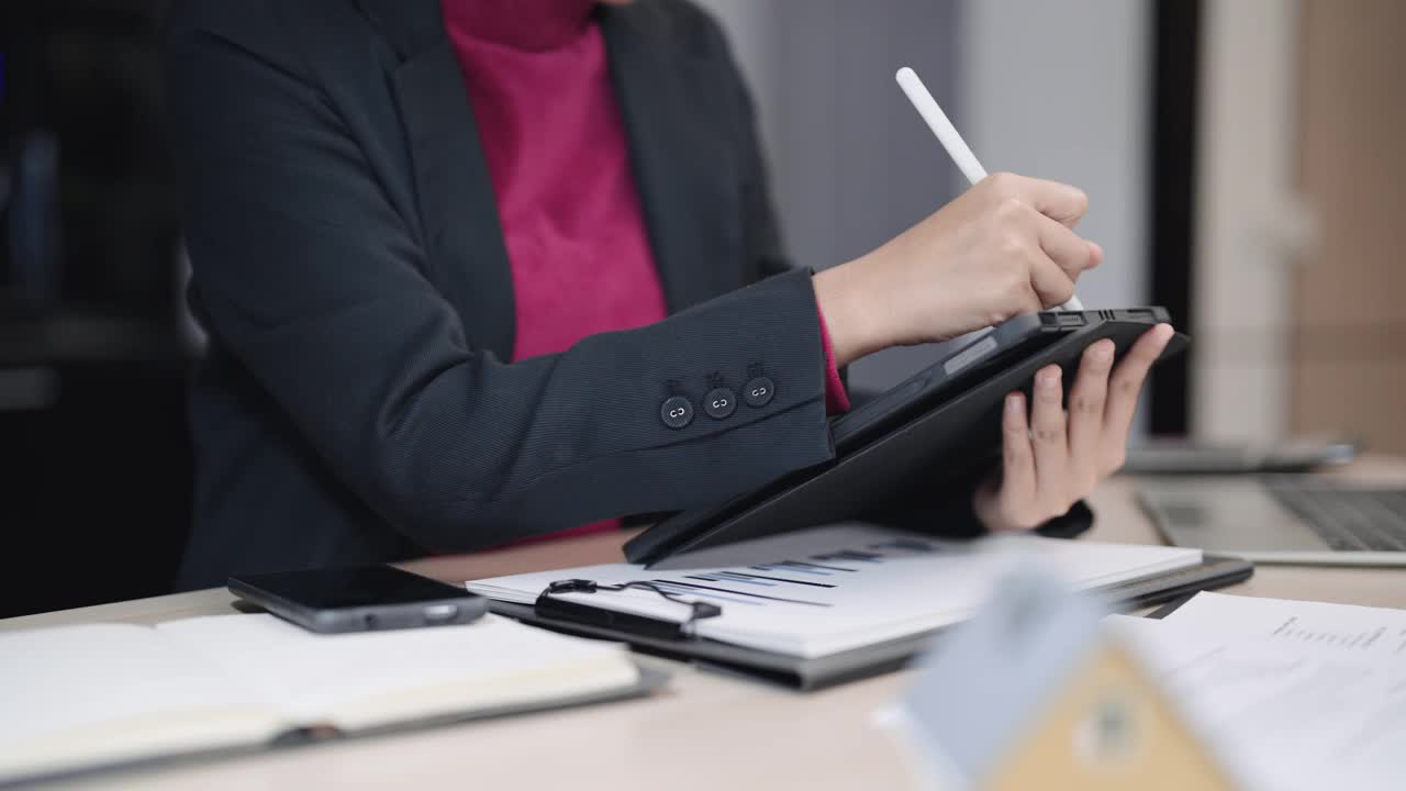 自信的亚洲女商人积极地在她的平板电脑上计划和输入她的商业项目，专注于她现代办公风格的工作桌旁视频素材