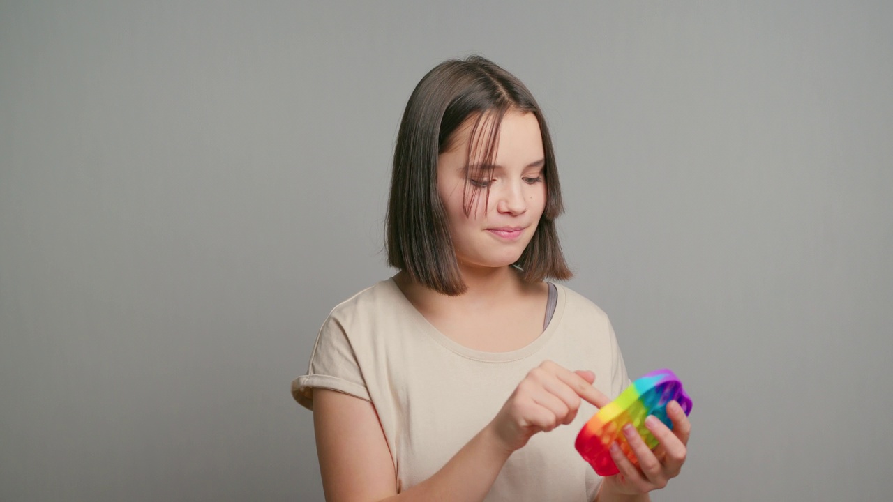 年轻的拉丁少女玩着pop-It儿童玩具，微笑着孤立在灰色的背景上。本空间视频素材