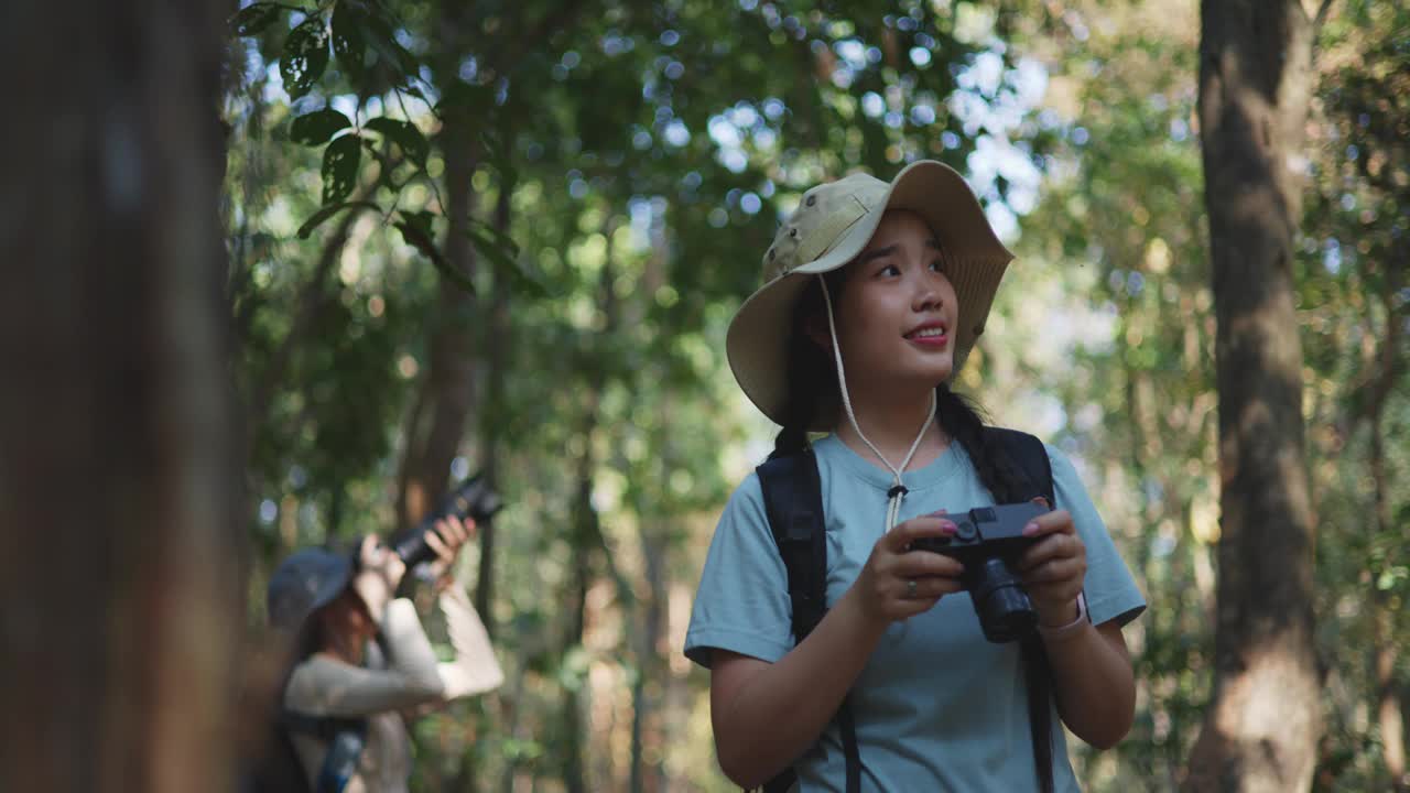 年轻的亚洲女背包客在秋天的森林里使用数码相机视频素材