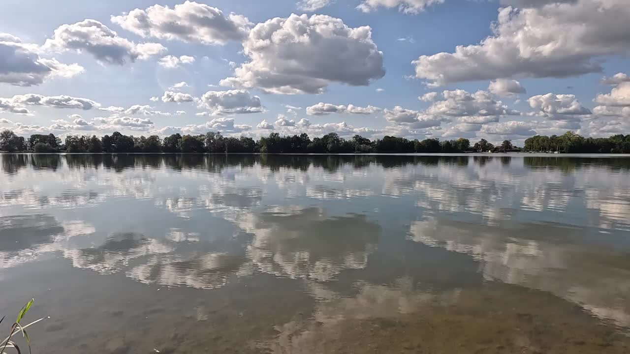 湖岸绿树成荫，宁静的湖水倒映着蓝天白云视频素材