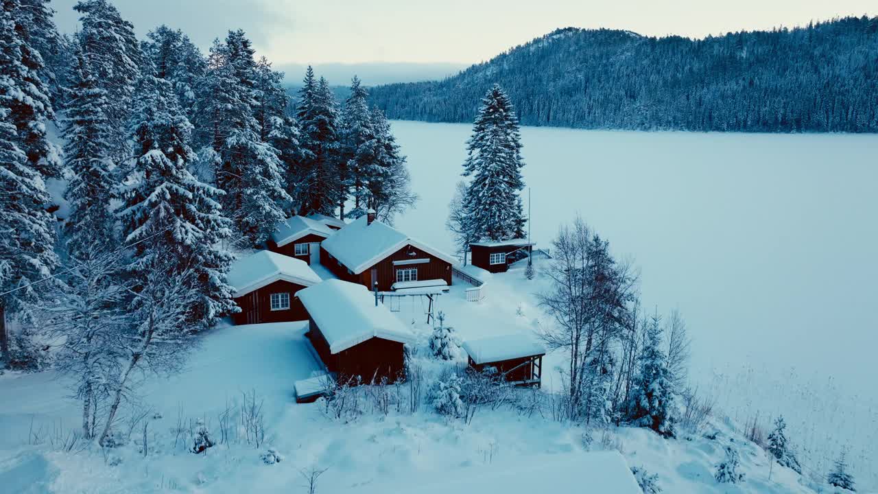 挪威小屋在山上与松树在冬天结冰的湖。-航拍视频素材