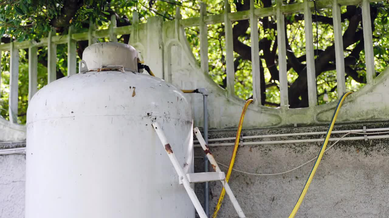 干净的储水罐用梯子和黄色的管道放在花园里，水箱在没有水供应的情况下抽水到房子里，水泵靠电工作视频素材