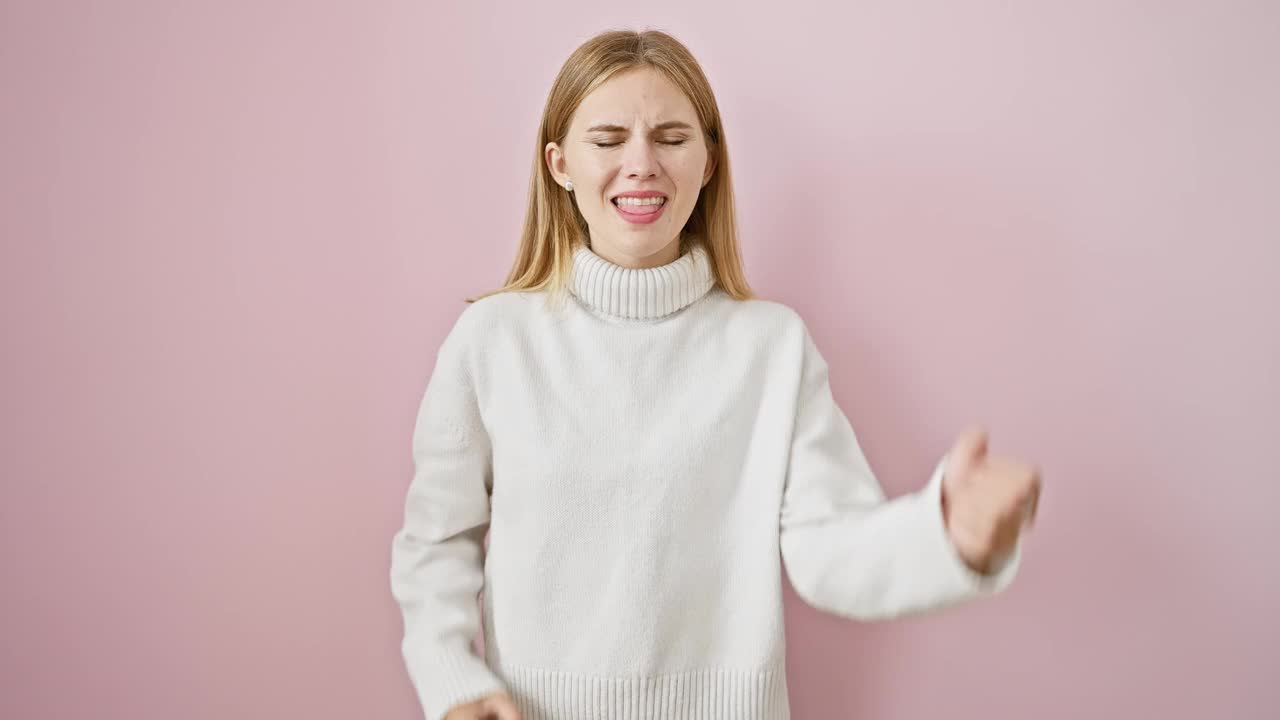 精力充沛的金发女孩尖叫在胜利的喜悦，沐浴在她激动人心的胜利!她兴高采烈地站在一个粉红色的、孤立的背景上，幸福到了极点。视频素材