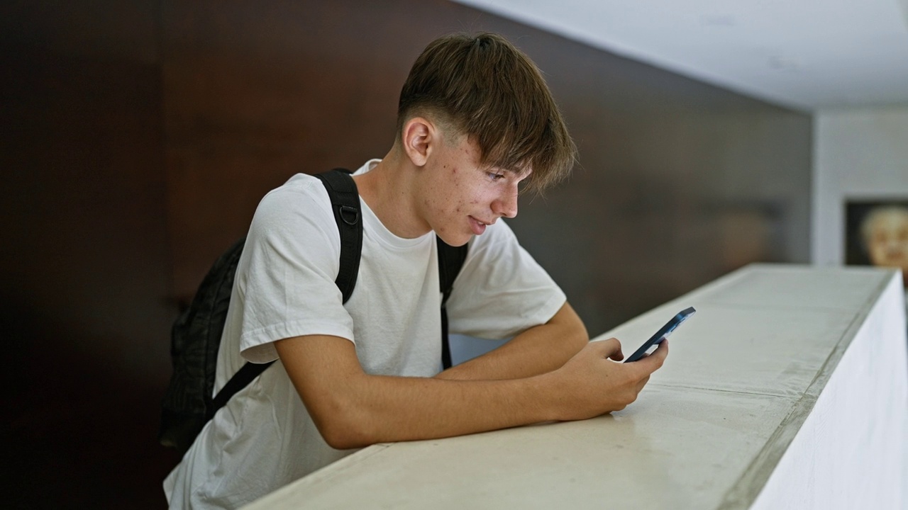 一名年轻的白人男学生在现代大学校园里用智能手机自拍。视频素材