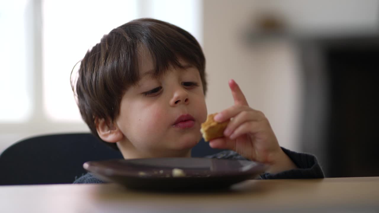 孩子坐在桌边吃面包当零食。一个四岁的小男孩正在吃碳水化合物食物视频素材