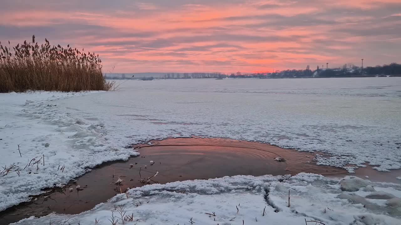 雪天里，粉红色的冬日夕阳映在冰冻的湖面上视频素材