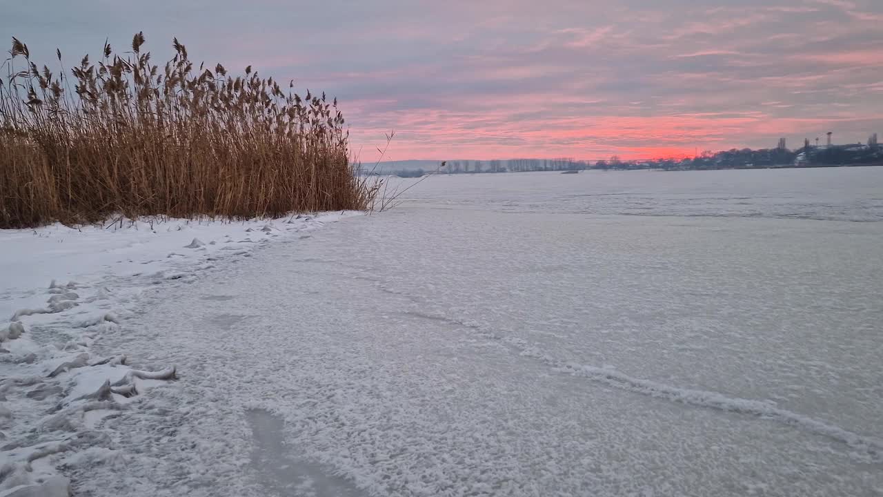 雪天里，粉红色的冬日夕阳映在冰冻的湖面上视频素材