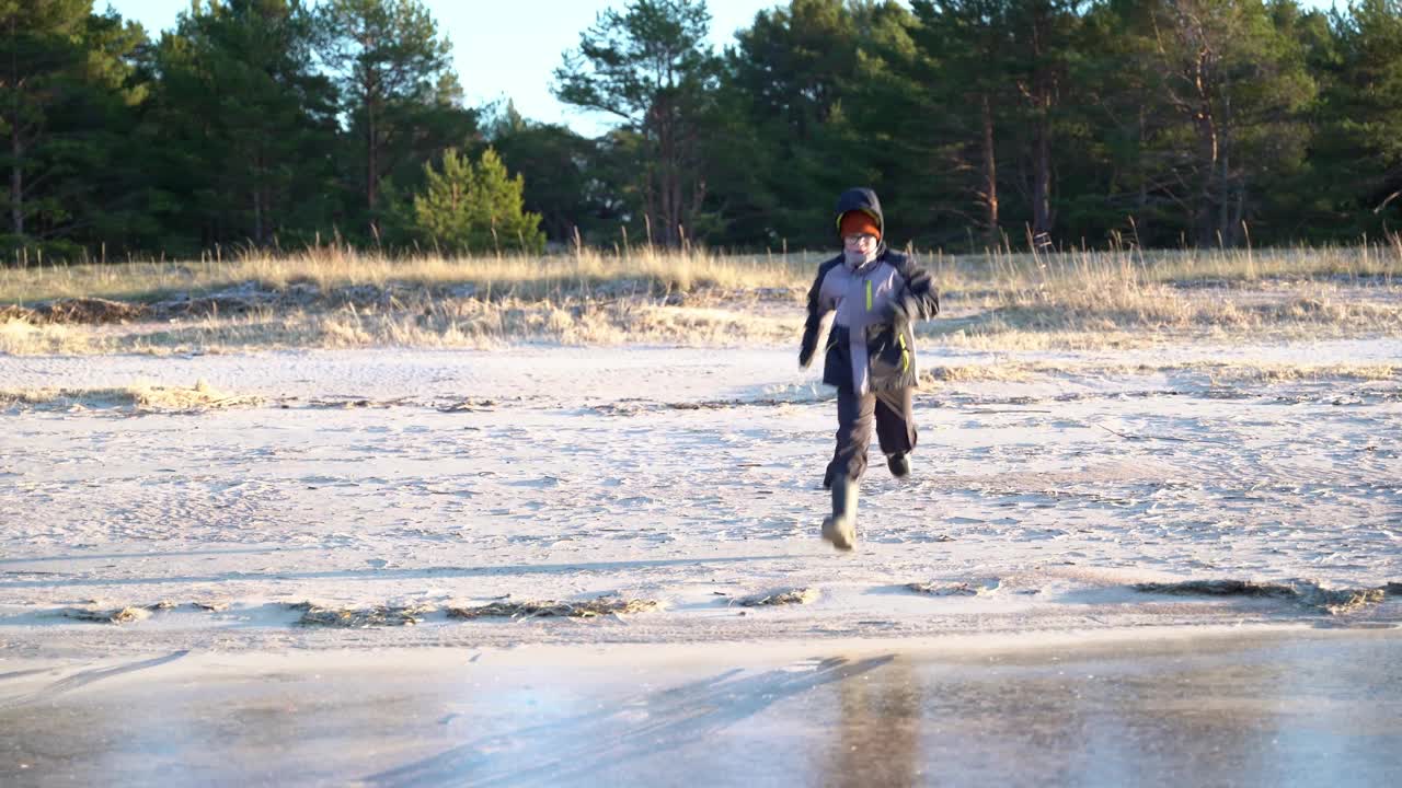 一个小男孩在冰雪覆盖的冬日沙滩上享受滑冰视频素材