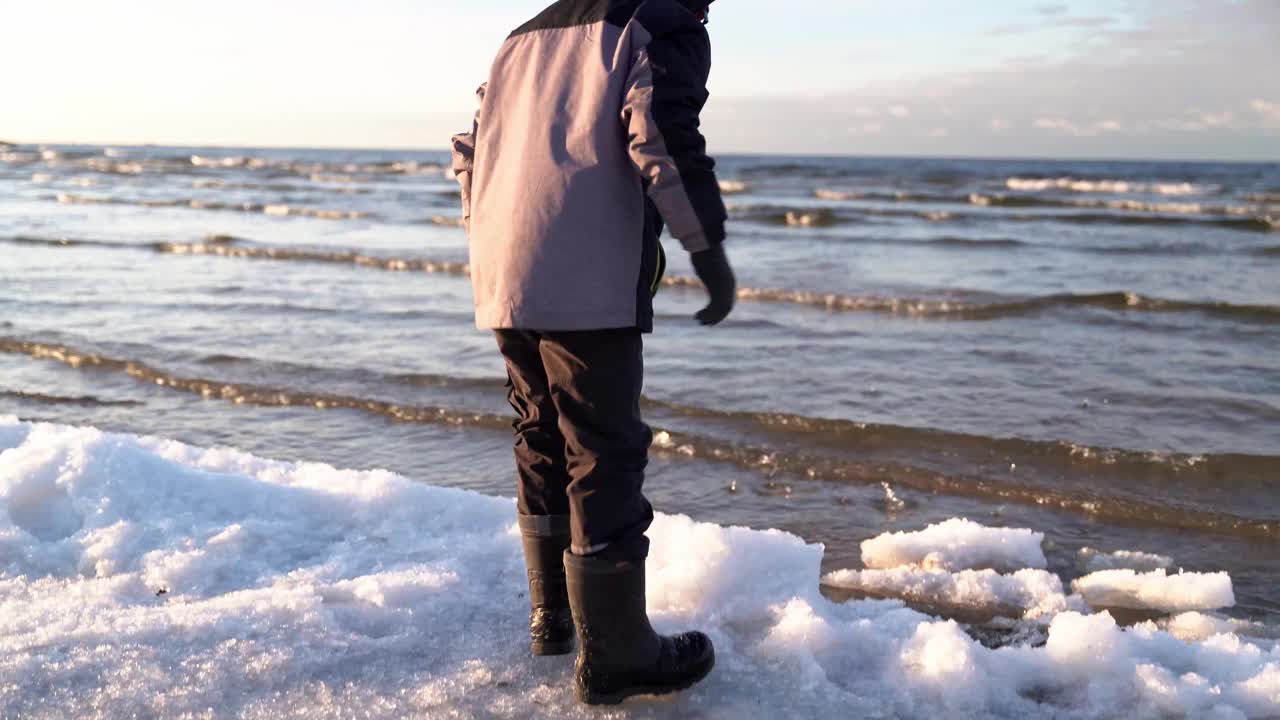 孩子们在海湾水域旁边的冬季海滩上与浮冰和雪玩耍视频素材