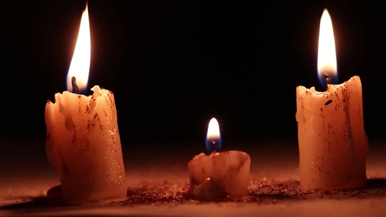 三支蜡烛在燃烧，背景中一名妇女的手在黑暗中放着一朵干玫瑰，哀悼和宗教，蜡烛的火焰视频素材