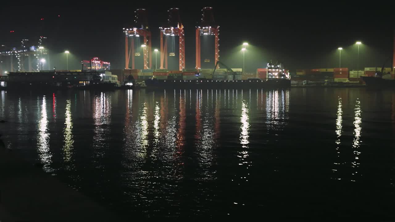 夜晚港口的景象与货物集装箱起重机，灯光反射在水中。月光下集装箱货物作业，吊车活跃。平静的水面映照出正在工作的集装箱起重机视频素材