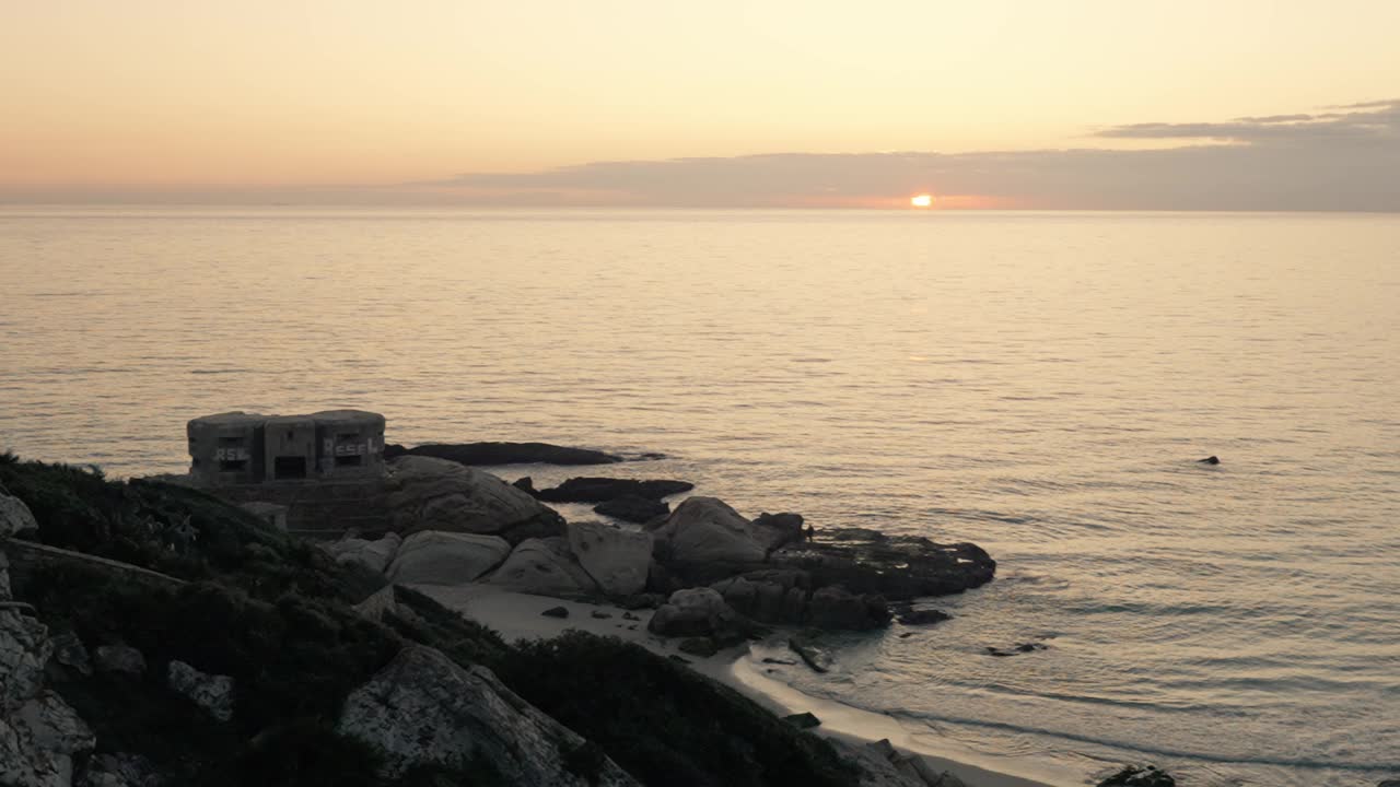 美丽的日落与橙色的天空在岩石海岸线与小废弃的建筑。视频素材