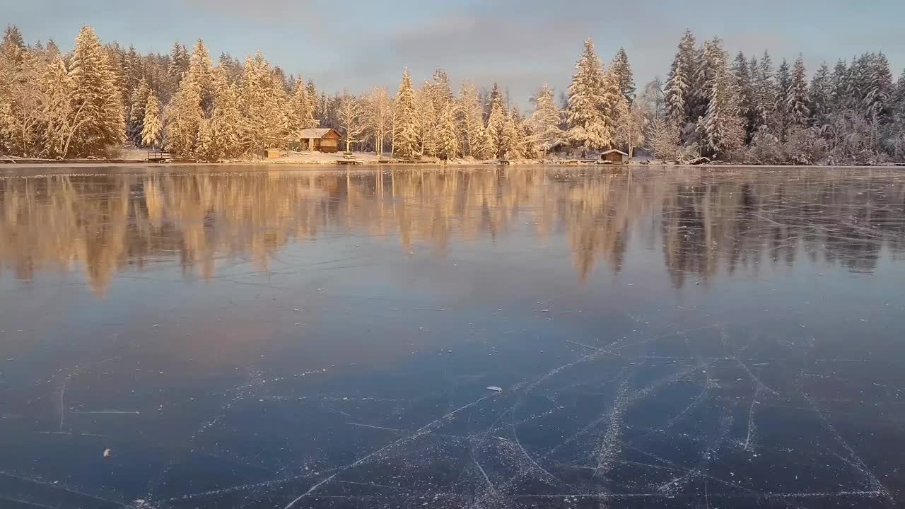 在阿尔卑斯山美丽的冰湖上滑冰，背景是木屋和白雪覆盖的树木。视频下载