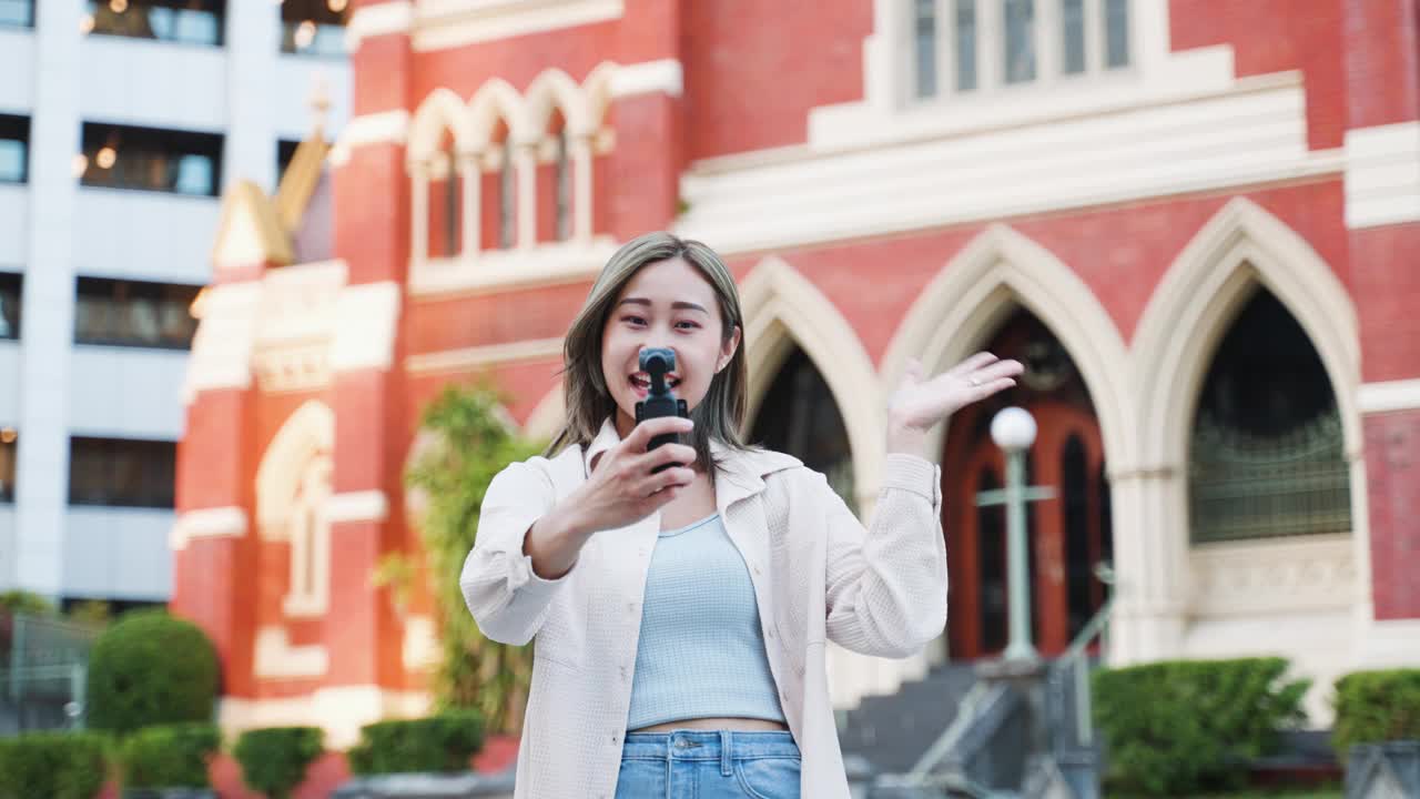 年轻的日本女子拿着相机说话，就像网红在城市旅行视频一样视频素材