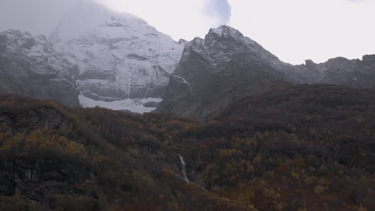 在山林间漫步。有创造力。树木环绕着巨大的山脉，游客们穿着暖和的衣服，在白色的天空下行走。高品质4k画面视频素材