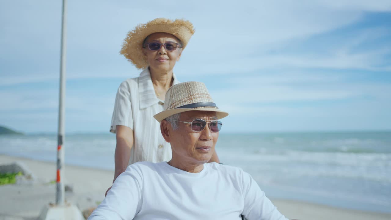 亚洲退休夫妇和坐在轮椅上的丈夫在海边放松。视频素材