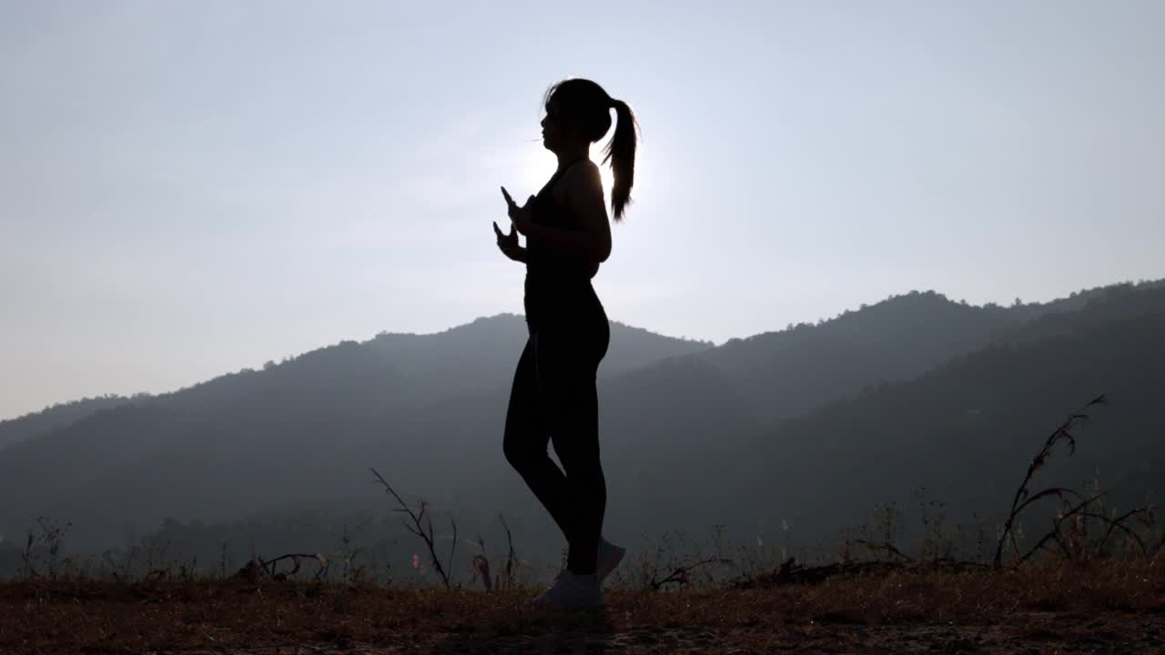 年轻女性在公园进行健身训练前的剪影。年轻女子在户外热身。她伸伸胳膊，望向别处。健康的生活方式和运动理念。视频下载