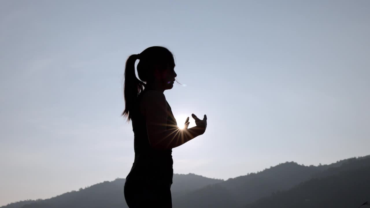 年轻女性在公园进行健身训练前的剪影。年轻女子在户外热身。她伸伸胳膊，望向别处。健康的生活方式和运动理念。视频下载