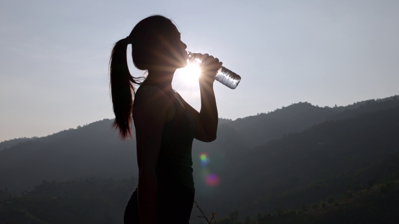 爱运动的女人在阳光明媚的日子里在户外喝水。年轻女性在公园健身训练前正在锻炼。健康积极的生活方式理念。视频下载