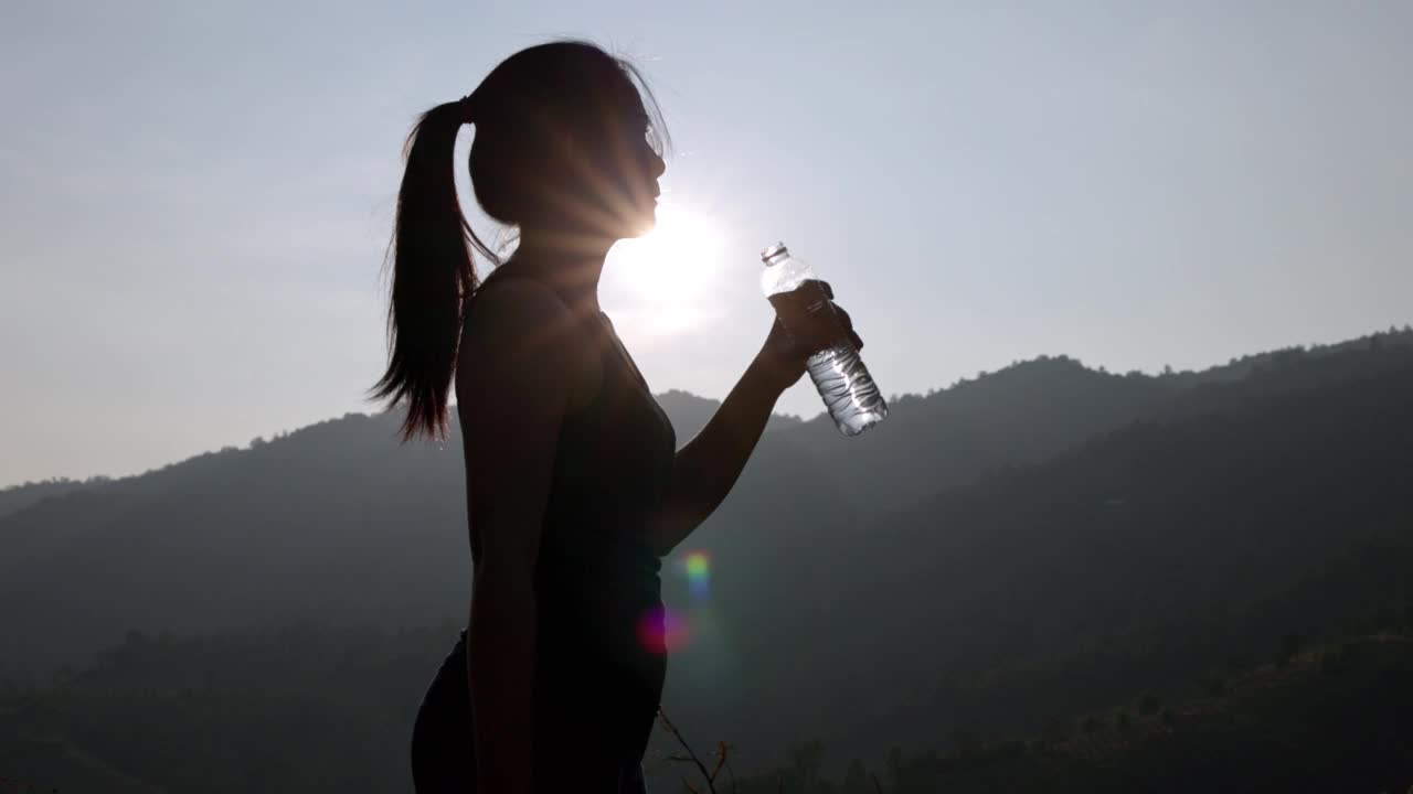 爱运动的女人在阳光明媚的日子里在户外喝水。年轻女性在公园健身训练前正在锻炼。健康积极的生活方式理念。视频下载