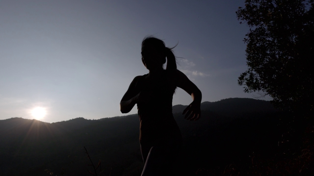 夕阳下身穿运动服的女子在山上慢跑的剪影。穿着运动胸罩在户外跑步的年轻亚洲女性。晚上锻炼身体。健康积极的生活方式理念。视频下载