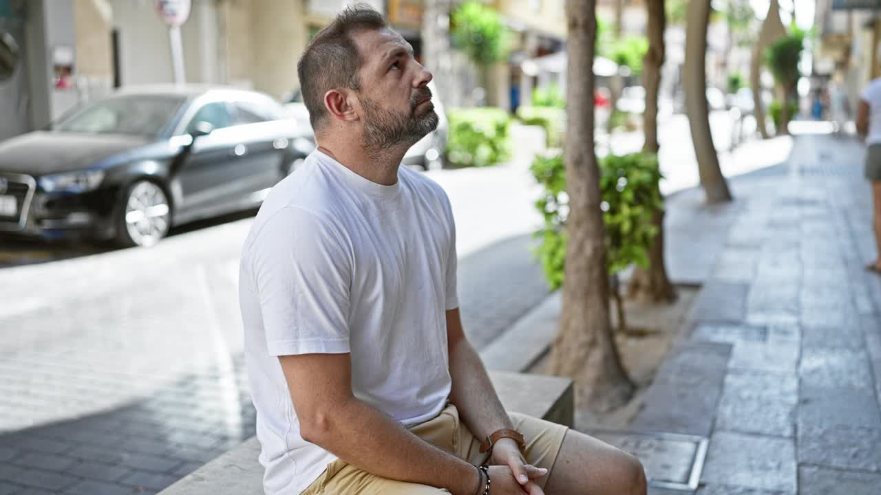 成熟的西班牙裔男子坐在城市环境中的长凳上查看手表时间视频素材