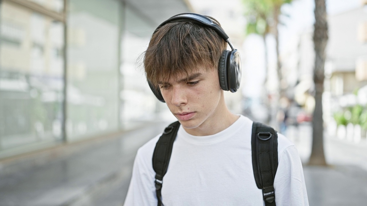 一位戴着耳机的年轻白人男性少年若有所思地走在城市街道上视频素材