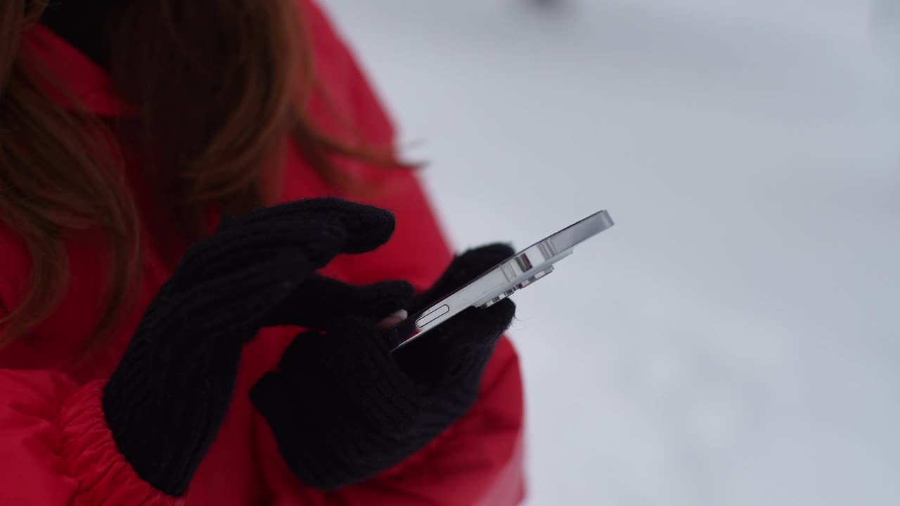 特写镜头显示，在下雪的公园里，一个不知名的女人戴着温暖的手套在智能手机屏幕上打字。女性特写在通讯应用中视频素材