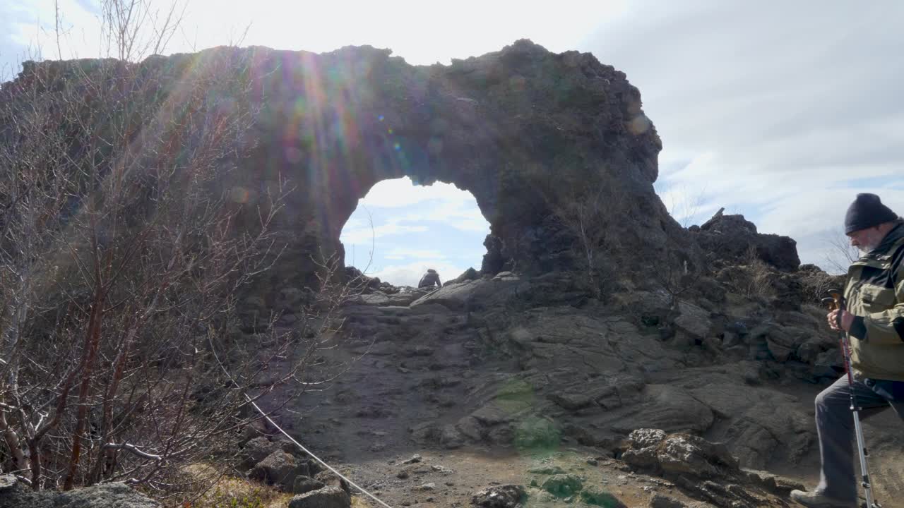 背着背包的徒步旅行者在冰岛的Dimmuborgir崎岖的地形上徒步旅行，在一个天然的石头拱门下，阳光透过视频素材