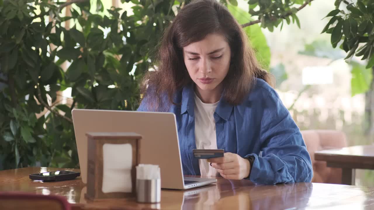 在绿植环绕的咖啡馆里，一个微笑的女人正在用笔记本电脑打电话视频素材