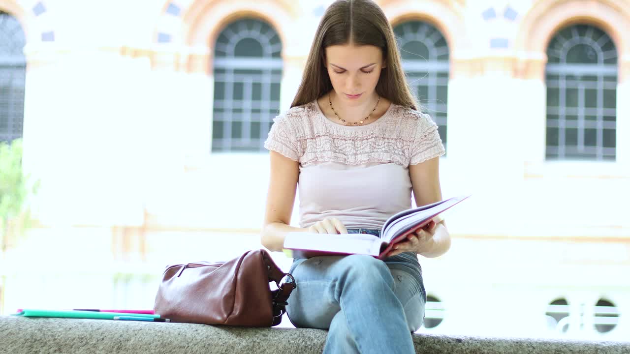 美丽的女大学生在公园的长椅上看书视频下载