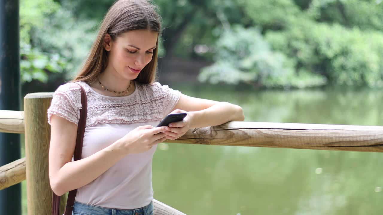 一名年轻女子在公园户外用智能手机拍照视频下载