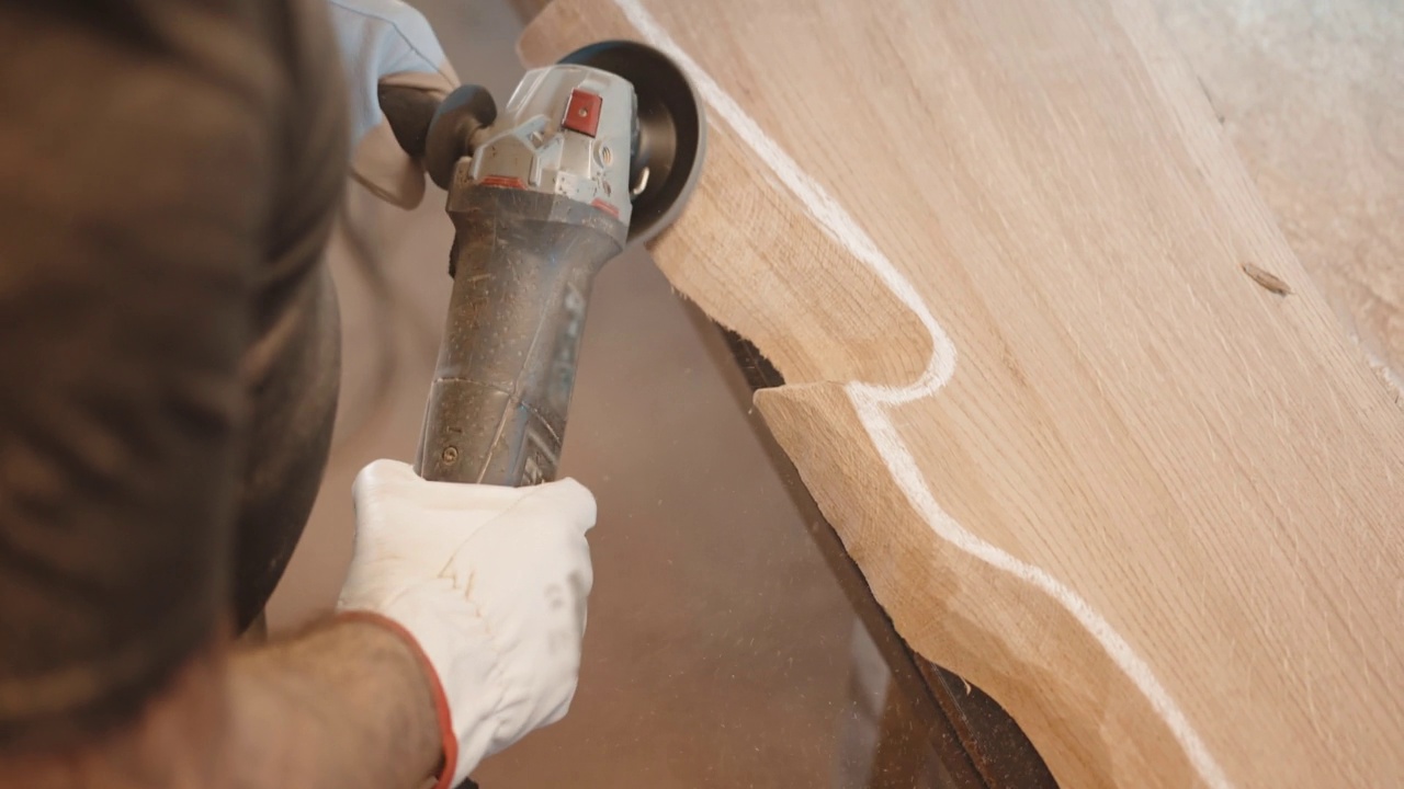 穿着防护服的专业木匠在工厂车间处理原木板，工匠沿着白色标记线用磨床磨木角，打磨机形成锯末视频素材
