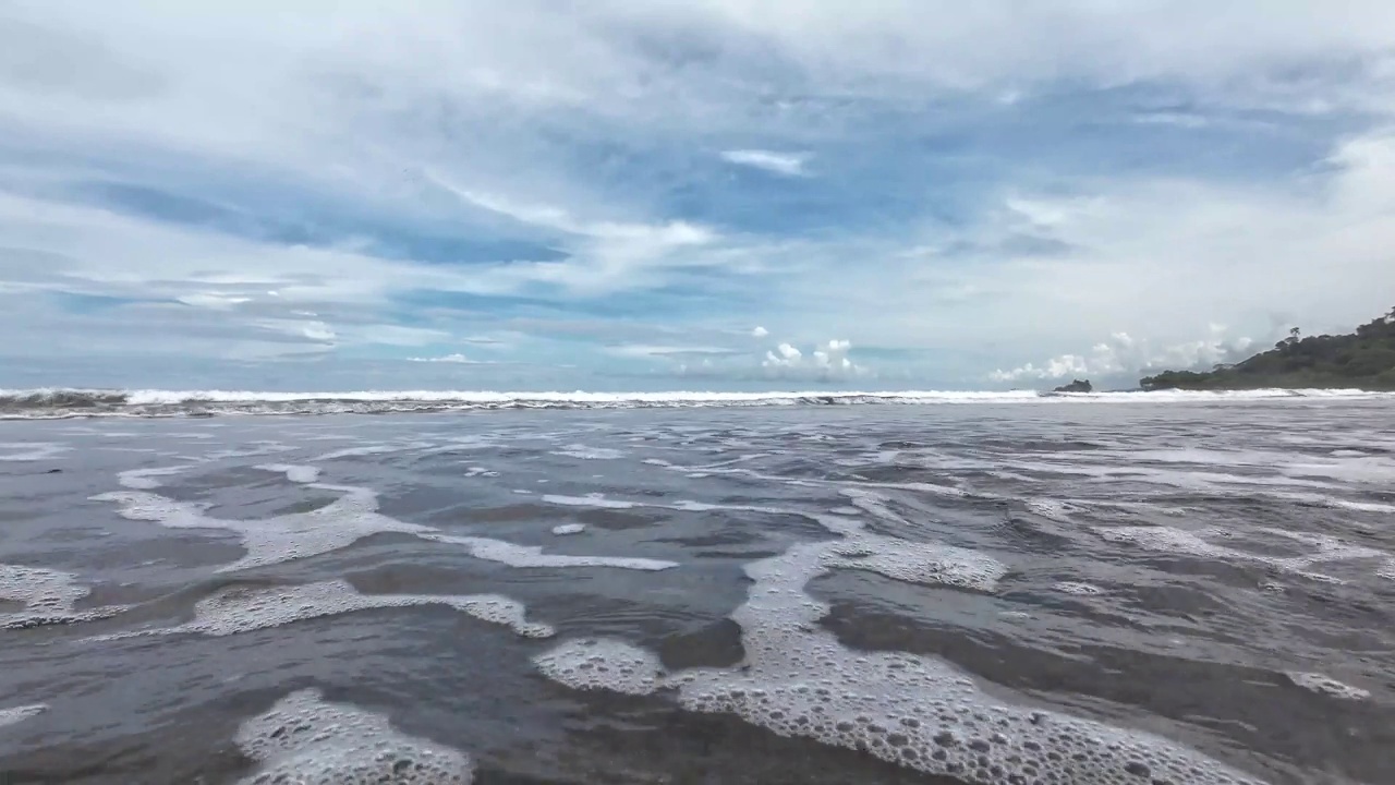 一个田园诗般的海滩视频-温柔的海浪在镜头前破碎，周围是明亮的蓝天和风景如画的云。一个欣赏大自然美景的好地方。本空间视频下载