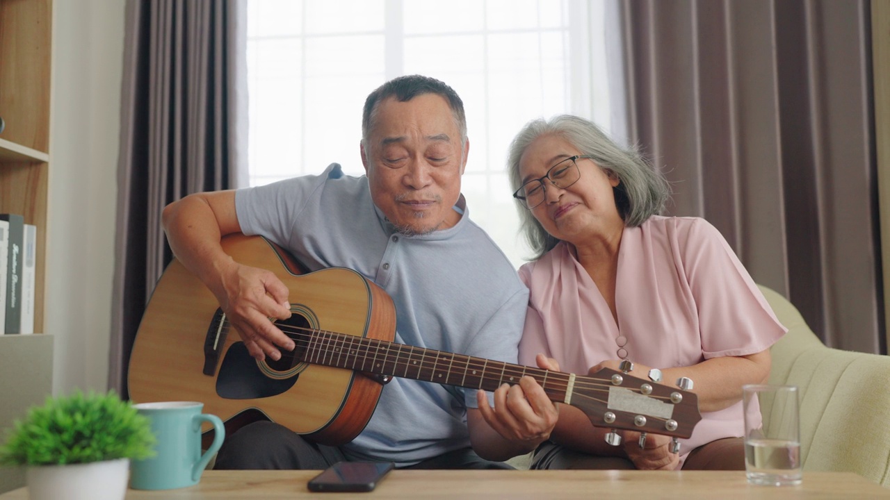 老年夫妇弹吉他，老年妇女风趣地听。坐在客厅里。视频素材