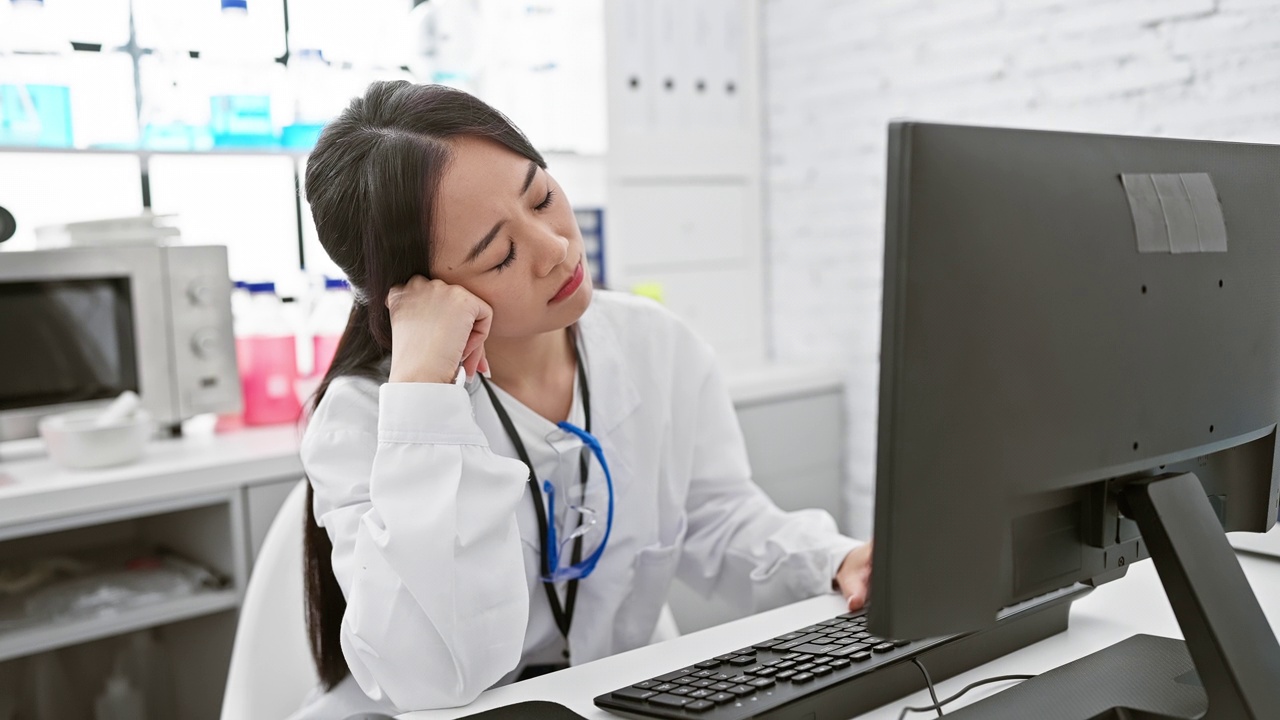 穿着白大褂的中国年轻女科学家，在实验室里摆姿势，累了却开心地做着梦，微笑着享受着宁静的小睡。视频素材