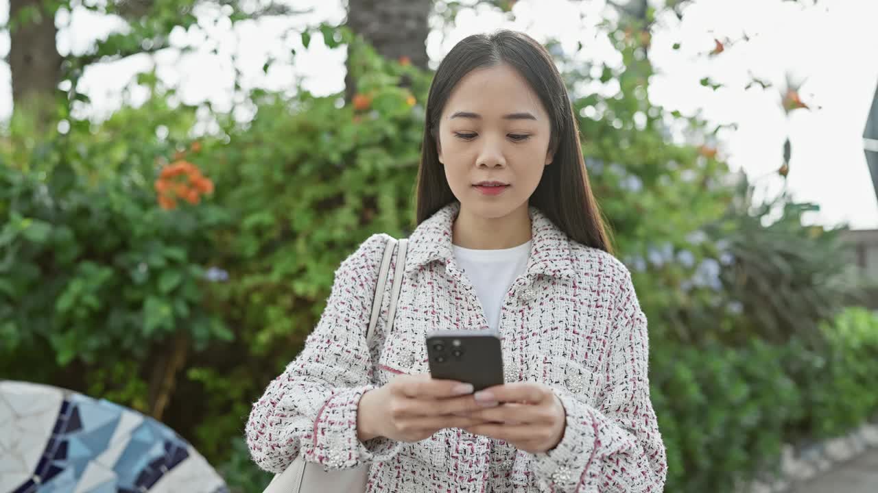 一位年轻的亚洲女性在绿树环绕的户外使用智能手机视频素材