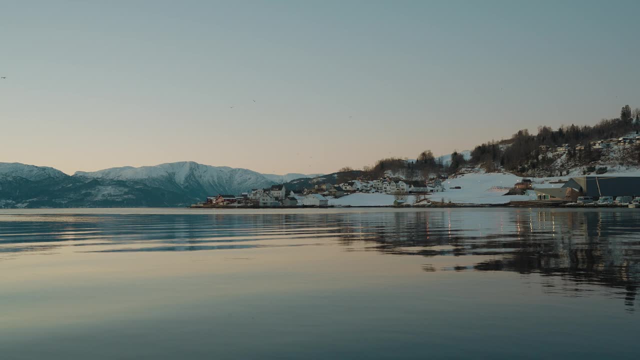 挪威的Ytre Samlafjorden的景色，以清澈的海水，横跨水面的雪山和冬雪中的家园为特色视频素材