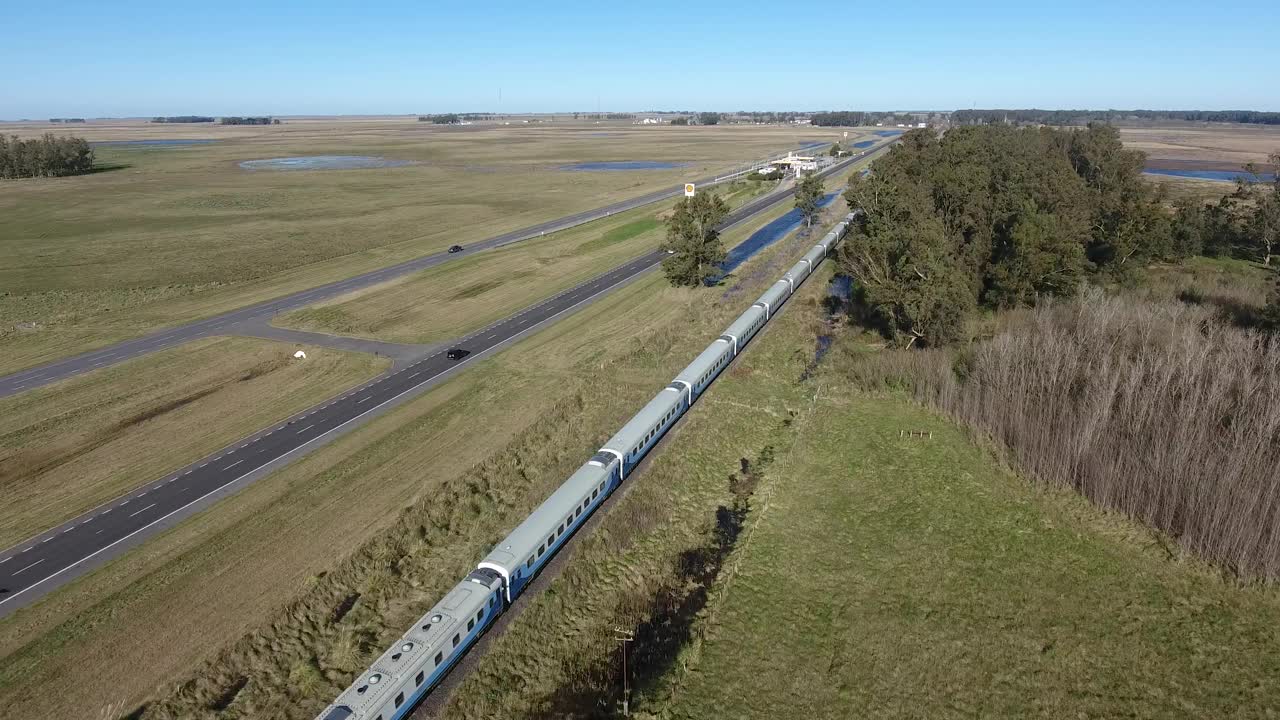 在布宜诺斯艾利斯郊区晴朗的天空中，一列火车沿着乡村的高速公路行驶视频素材