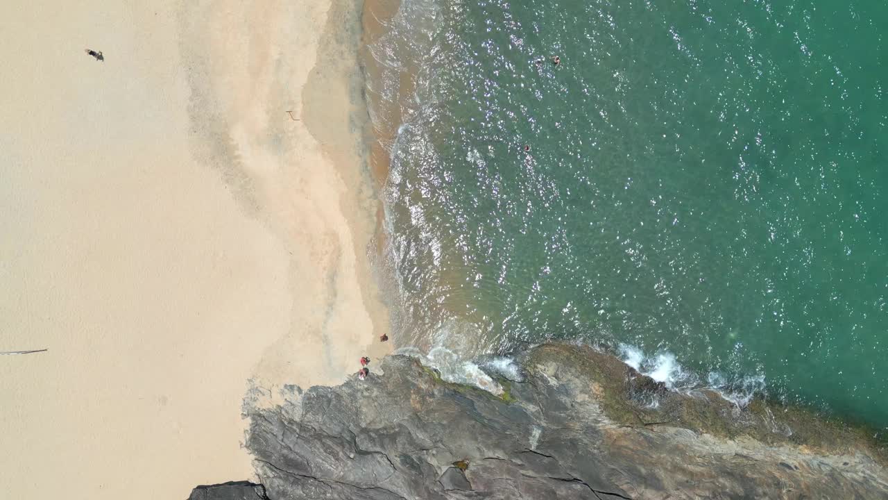 海滩的空中移动视图，旁边是山。有人在水里。视频下载