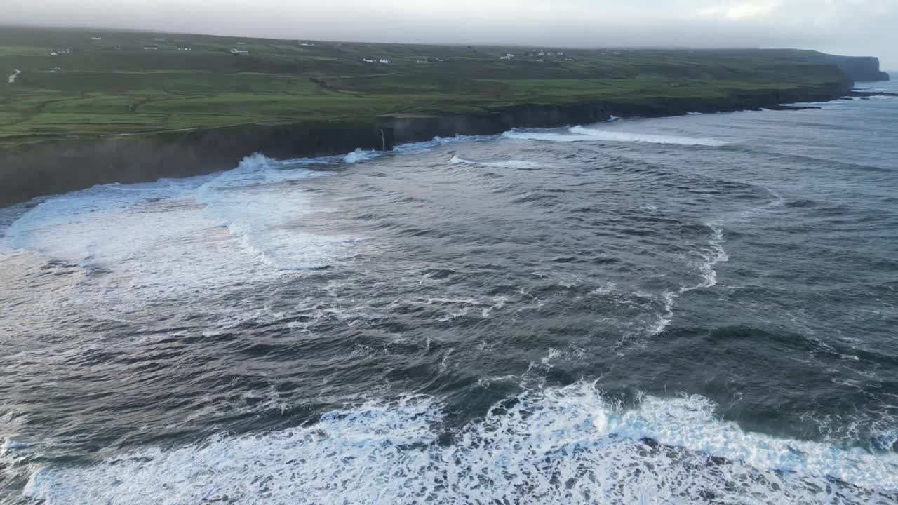 从空中俯瞰，狂暴的大西洋海浪冲击着爱尔兰杜林的悬崖，背景是葱郁的绿色田野视频素材