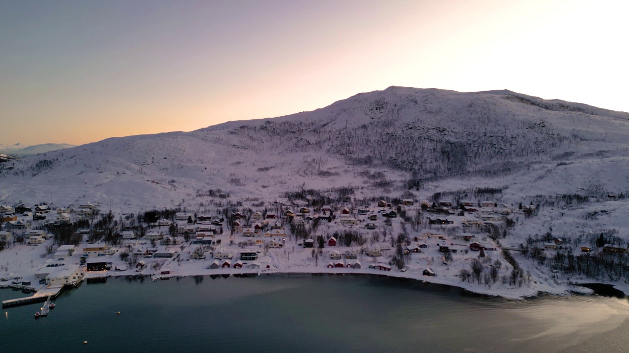 日出时，海边白雪覆盖的村庄，厄斯峡湾的地平线上有温暖的光线视频素材