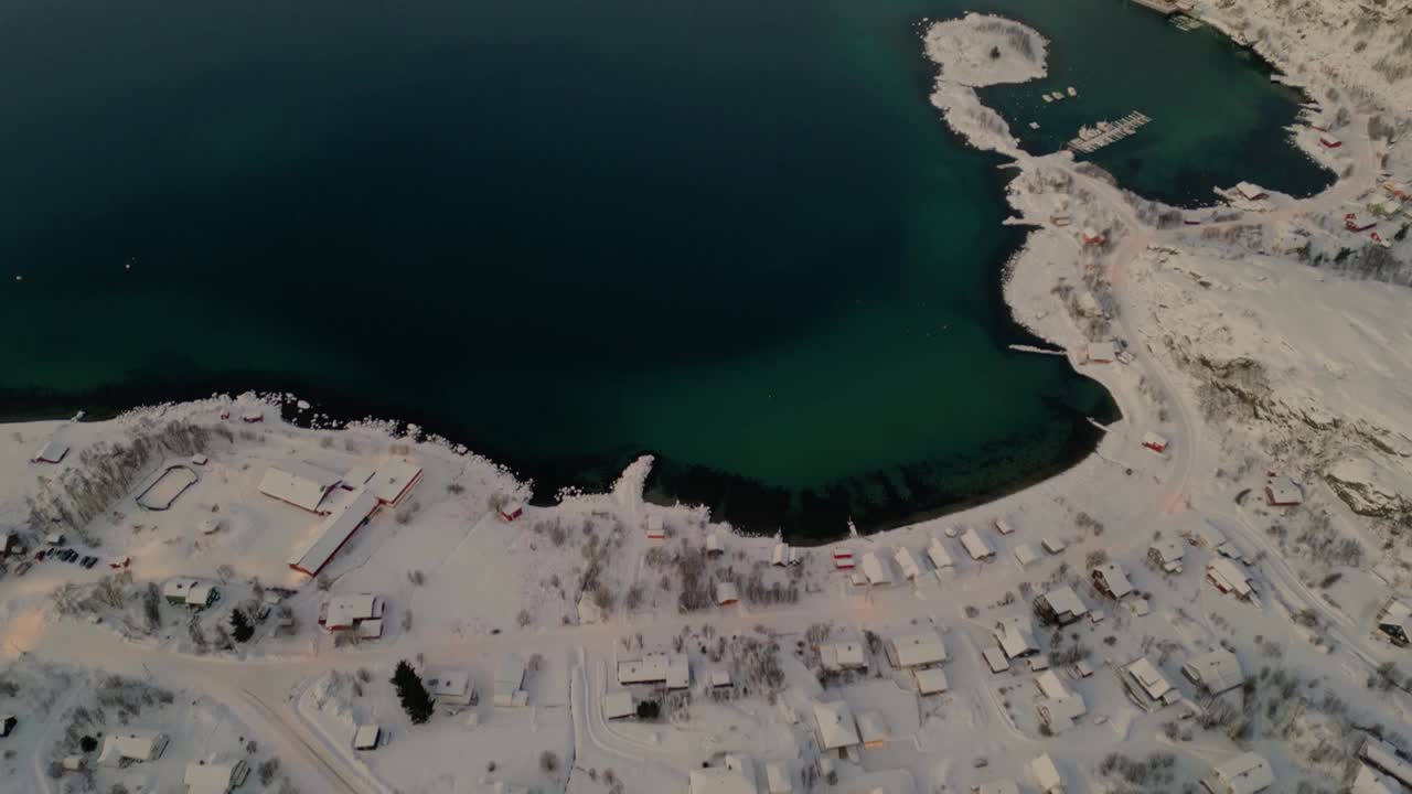 从积雪覆盖的沿海村庄到峡湾美丽的翡翠水域的全景鸟瞰图视频素材