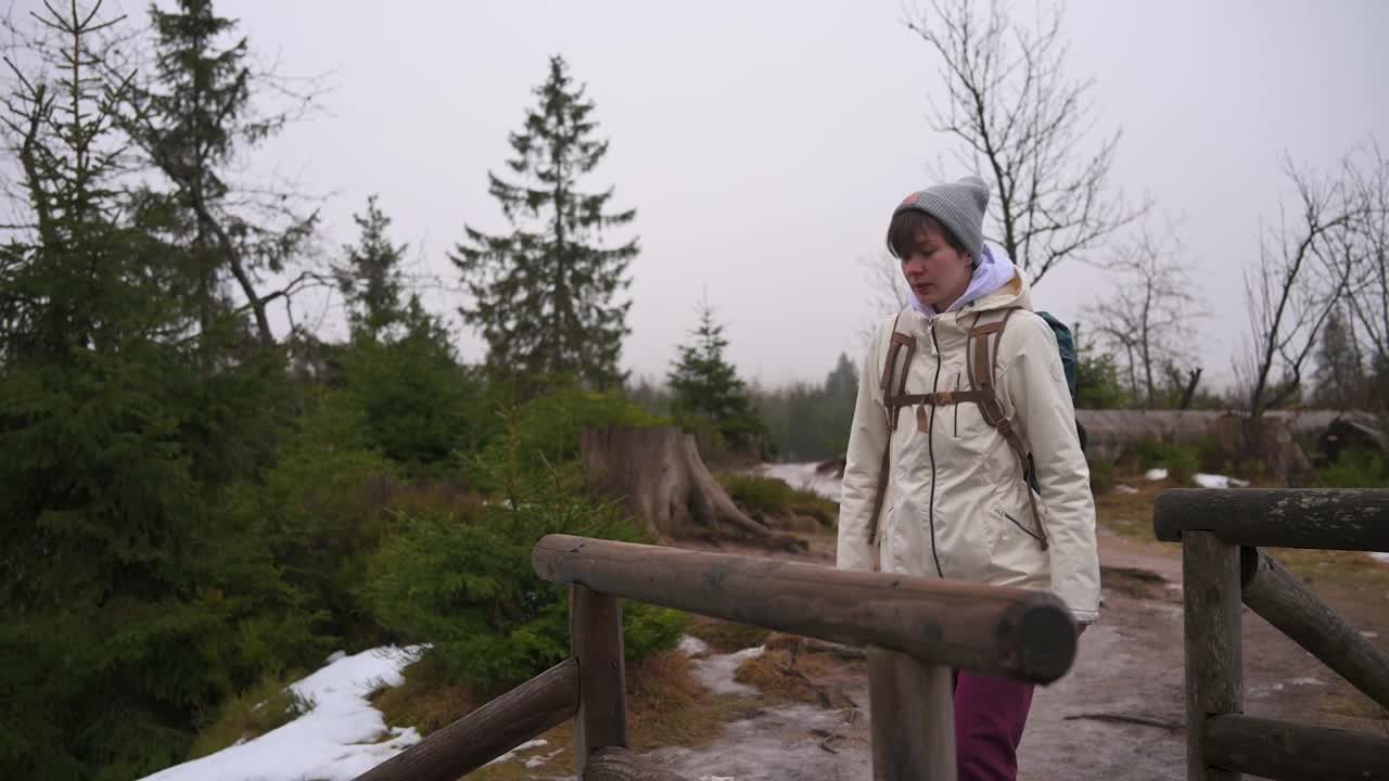 在白雪皑皑的森林里，一个体贴的女人倚在木栏杆上视频素材