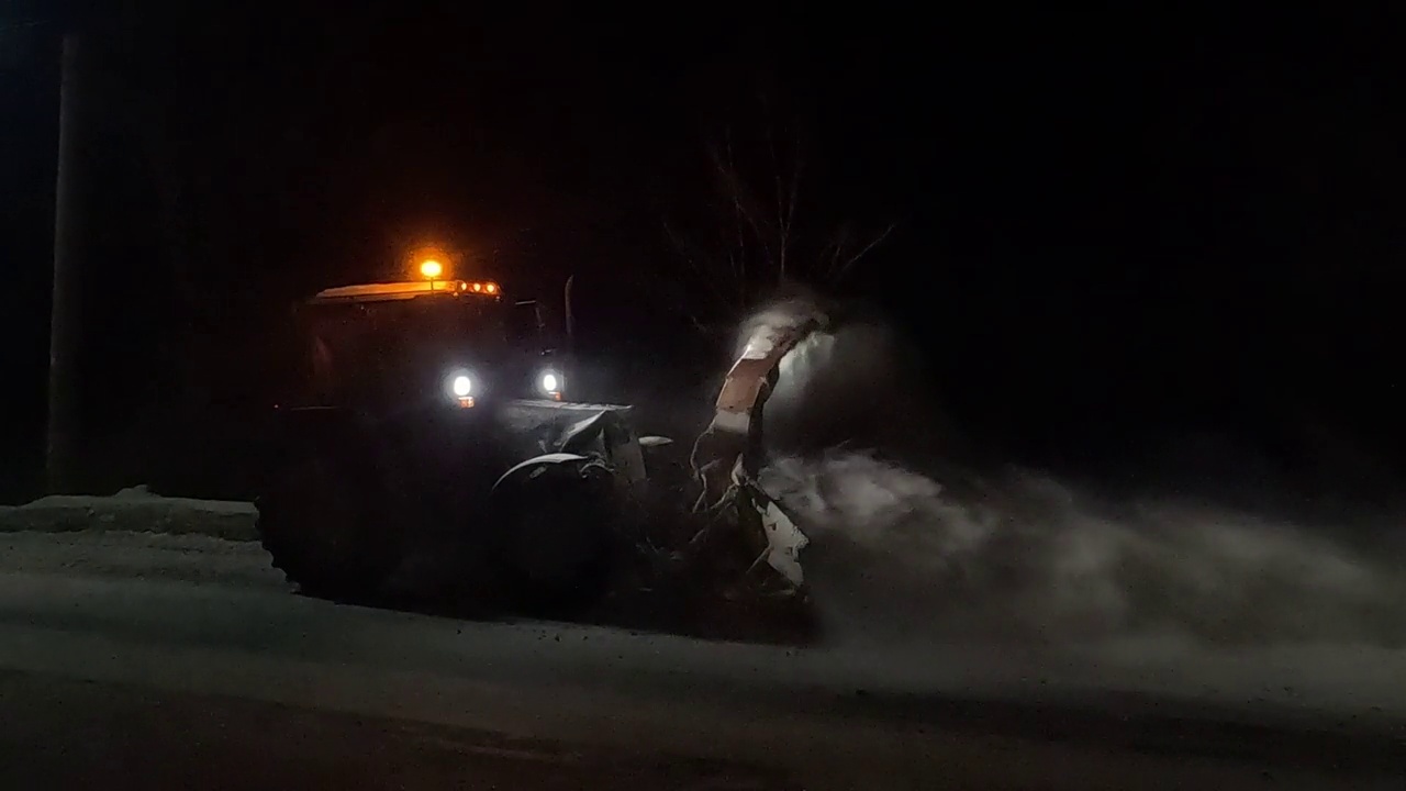 以拖拉机形式出现的除雪设备，在夜间作业，将道路上的雪扔进沟里视频下载