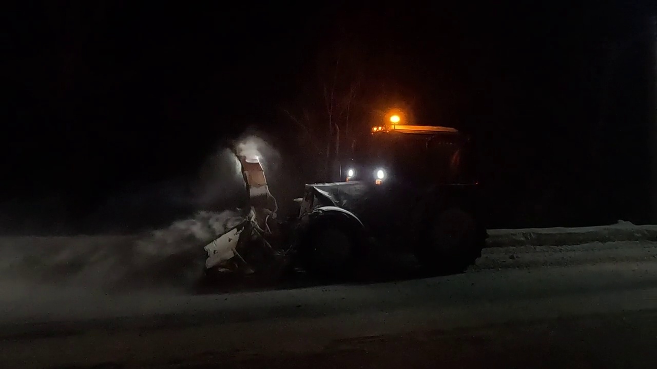 以拖拉机形式出现的除雪设备，在夜间作业，将道路上的雪扔进沟里视频下载