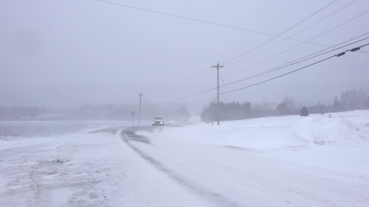 暴风雪中行驶在乡村道路上的汽车。危险的驾驶条件。视频下载