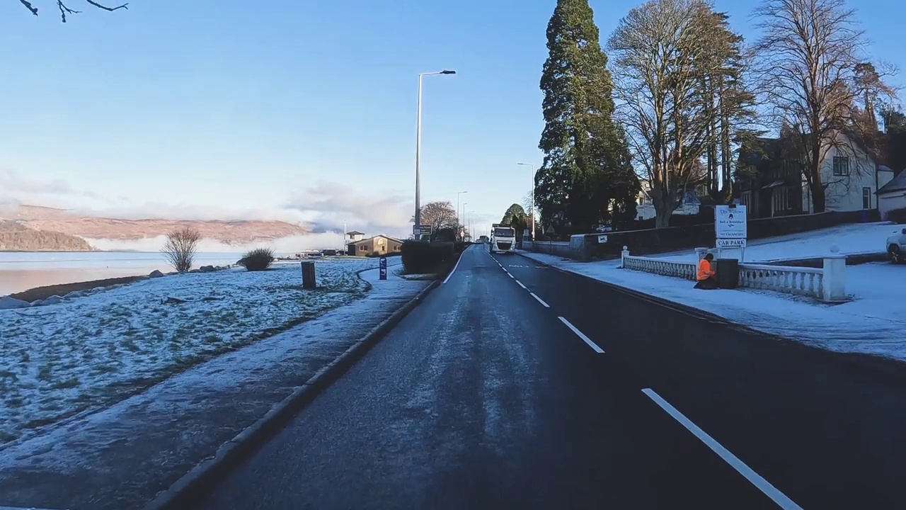 蜿蜒的道路两旁有积雪，通向宁静的苏格兰风景，湛蓝的天空，冬天，汽车的视角视频素材