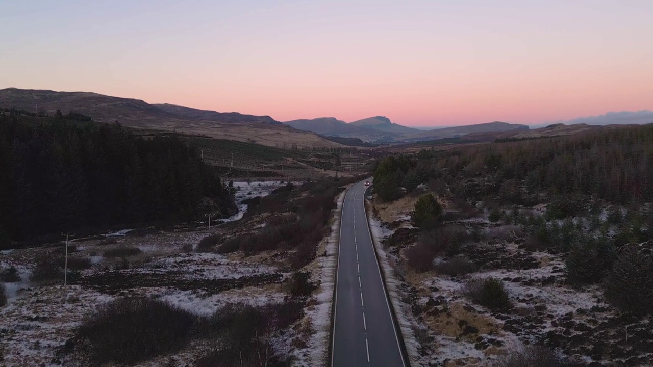 暮色笼罩着一条孤独的道路，穿过崎岖的地形，雪片，宁静的风景，鸟瞰视频素材