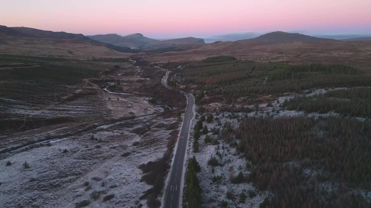 蜿蜒的道路穿过白雪皑皑的格伦科在黄昏，展示宁静的苏格兰高地，鸟瞰视频素材